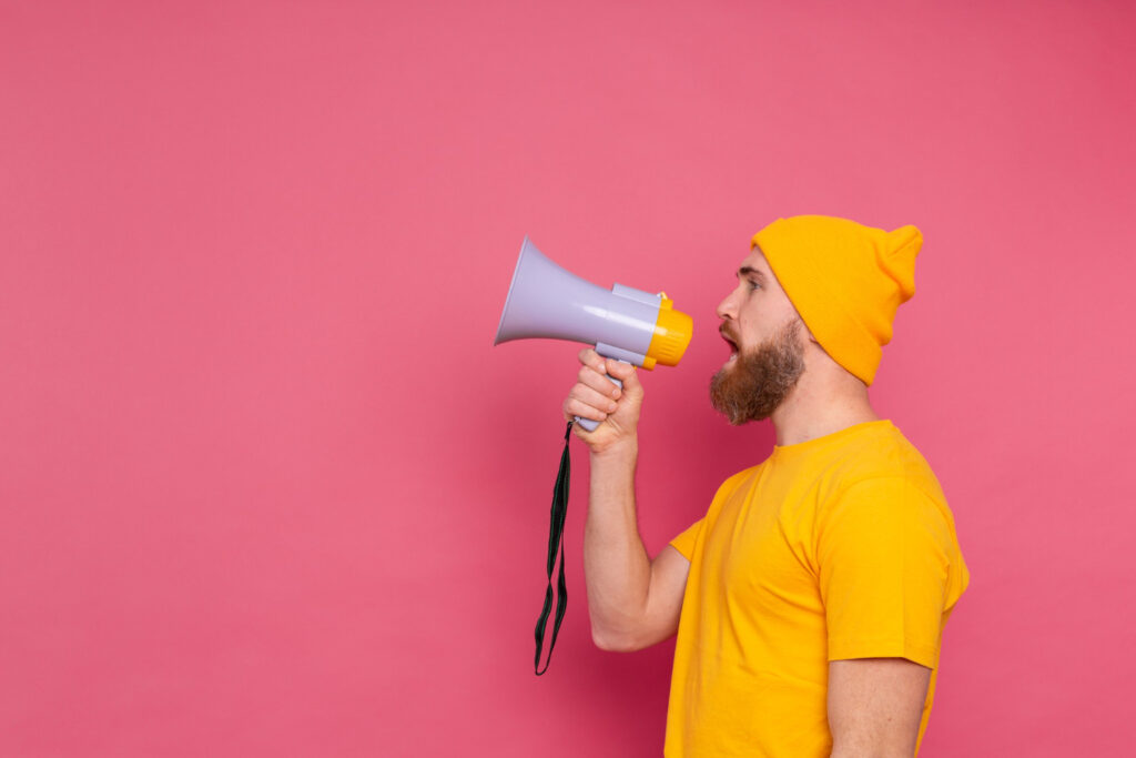 Homem com roupas amarelas segurando um megafone branco em um fundo rosa para anunciar um CTA